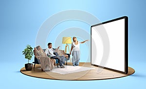 Young positive family in pajamas, man, woman and children sitting on sofa and looking at giant 3D model of tablet with