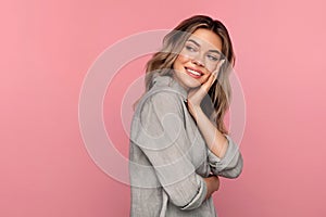 Young happy woman look aside holding hand on cheekbone with pleasant positive smile over pink wall photo