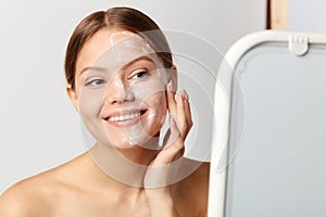 Young positive girl applying cream on face photo