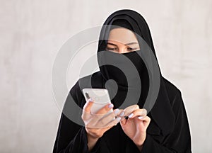 young positive girl with her face covered by burka holds phone in her hands and surf Internet