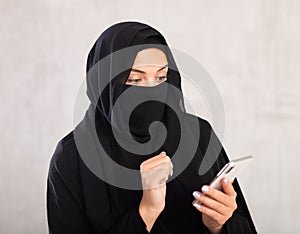 young positive girl with her face covered by burka holds phone in her hands and surf Internet