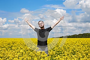 A young positive guy stands in a yellow field rejoicing and stretches his hands to the sky