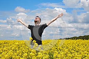 A young positive guy stands in a yellow field rejoicing and stretches his hands to the sky