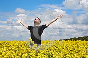A young positive guy stands in a yellow field rejoicing and stretches his hands to the sky
