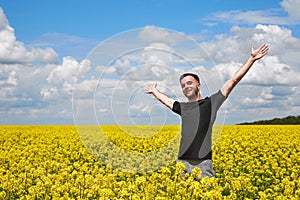 A young positive guy stands in a yellow field rejoicing and stretches his hands to the sky