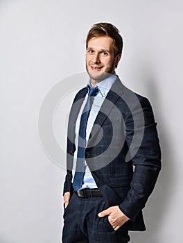 Young positive handsome business man in official costume suit and tie standing and smiling over light grey wall