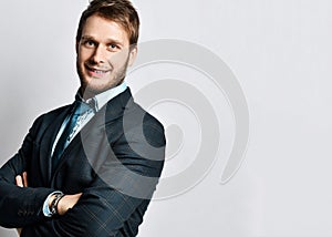 Young positive handsome man in official costume and tie standing and smiling over light grey wall background