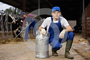 Young positive male farmer with milk metalic can near stall with cows during work on dairy farm