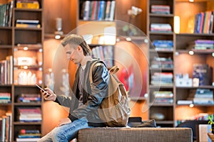 Young positive man picking new book on shelves in bookstore