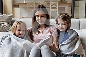 Young positive mommy sitting on floor with kids, reading story.