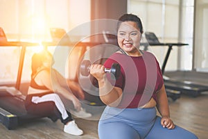 Young, Positive, Smiling, Cheerful overweight woman training with dumbbells in gym. Fat woman in sportswear doing fitness exercise