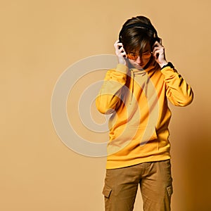 Young positive teen boy in yellow hoodie, sunglasses and headphones standing and smiling