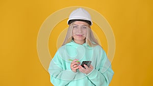 Young positive thinking girl builder in helmet with phone and pen in hands