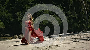 Young positive woman with blonde hair in elegant fluttering long red dress