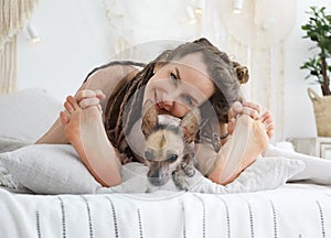 Young positive woman lying on the bed and having fun with her dog xoloitzcuintli