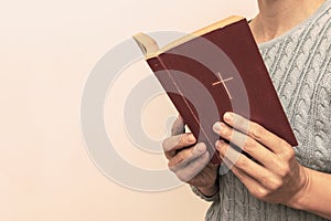 Young praying christian woman`s hands holding holy bible with a cross on a cover