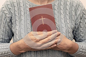 Young praying christian woman`s hands holding holy bible with a cross on a cover