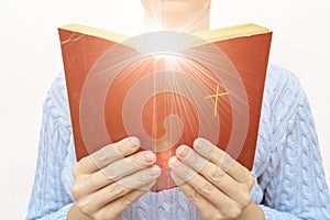 Young praying christian woman`s hands holding holy bible with a cross on a cover