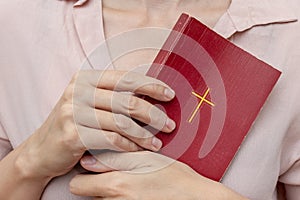 Young praying christian woman`s hands holding holy bible with a cross on a cover