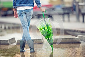 Young pre-teen girl stands with an umbrella in puddle after spring or summer rain