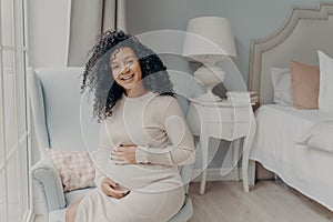 Young pregnant afro american woman in white dress posing in living room