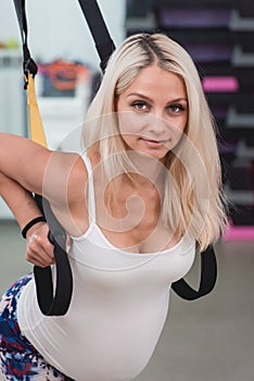 Young pregnant attractive woman training with trx fitness straps in the gym`s studio