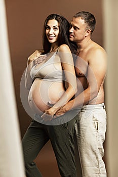 A young pregnant brunette woman is hugging with a torso man. Waiting for birth and tenderness.