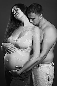 Young pregnant couple hugging and smiling. Love and tenderness. Waiting for a miracle. Black and white portrait.