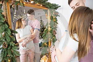 Young pregnant couple in the mirror. Christmas decorations. Pregnancy, winter holidays and people concept