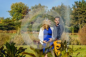 Young pregnant couple sitting on yellow leaves in the park