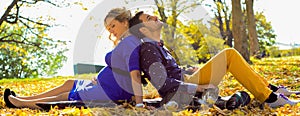 Young pregnant couple sitting on yellow leaves in the park