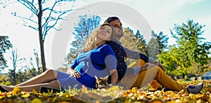 Young pregnant couple sitting on yellow leaves in the park