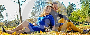 Young pregnant couple sitting on yellow leaves in the park