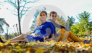 Young pregnant couple sitting on yellow leaves in the park