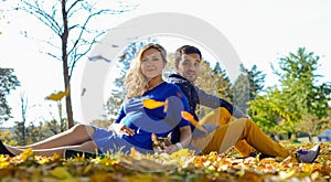 Young pregnant couple sitting on yellow leaves in the park