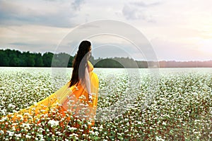 Young pregnant girl in a bright fiery dress walks on a flowering field of buckwheat