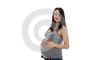 Young pregnant girl with dark hair touching her big belly and looking at the camera isolated on white background