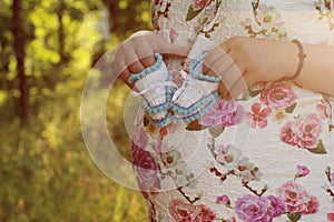 Young pregnant girl. Hands of a pregnant girl holding a close-up of baby booties in the parkr