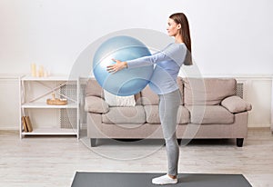 Young pregnant girl holding yoga ball at home