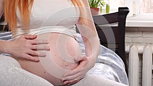 A young pregnant girl is stroking her big pregnant belly.