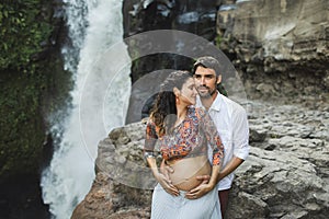 Young pregnant happy couple with view of waterfall. Pregnancy travel lifestyle.