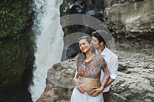 Young pregnant happy couple with view of waterfall. Pregnancy travel lifestyle.