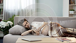 Young pregnant lady having rest on couch, hugging teddy bear, maternity care