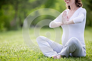Young pregnant model meditating on grass lawn. Close-up