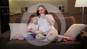 Young pregnant mother and boy-son spend time together in evening, watch terrible terrible movies on TV, mother covers