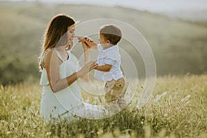 Young pregnant mother with her cute little boy in the field on beautiful sunny day