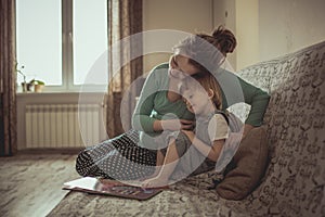 young pregnant mother and son reading a book on sofa, lifestyle,