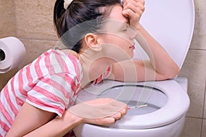 Young pregnant tired woman with pain is vomiting in toilet sitting on the floor at home.