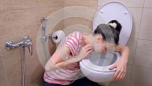 Young pregnant tired woman is vomiting in toilet sitting on the floor at home.