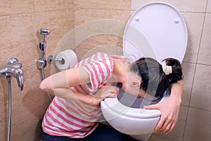 Young pregnant tired woman is vomiting in toilet sitting on the floor at home.